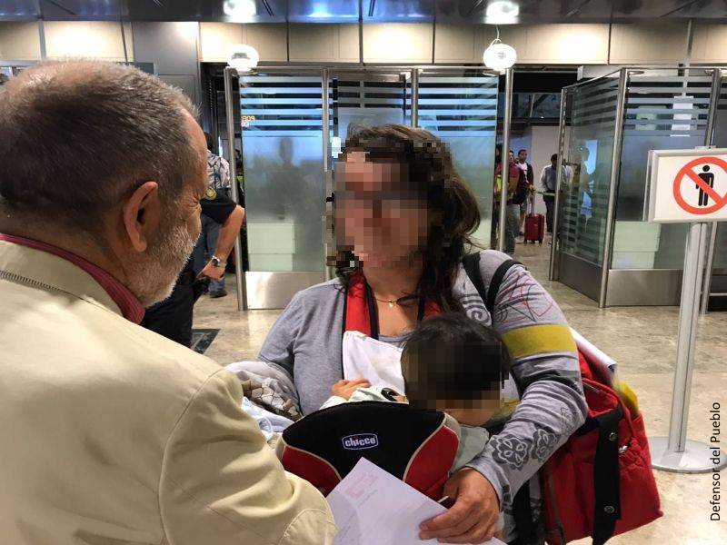 Francisco Fernández Marugán (Defensor e.f.) charla con una mujer que lleva un bebé en una mochila (ambos rostros pixelados) en el aeropuerto